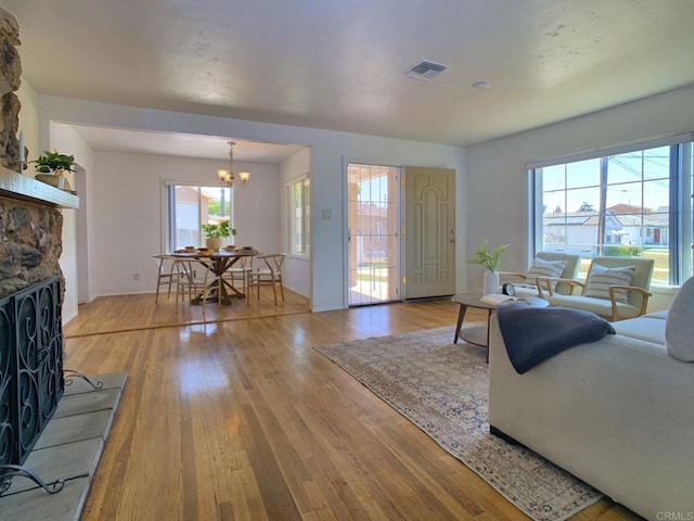 living room with light wood-type flooring, a chandelier, a fireplace, and baseboards