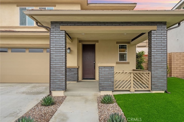 view of exterior entry with stucco siding, covered porch, and brick siding