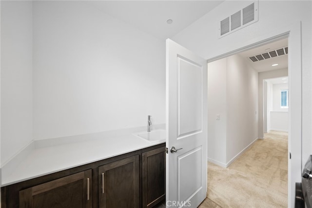 hallway with light colored carpet, a sink, and baseboards
