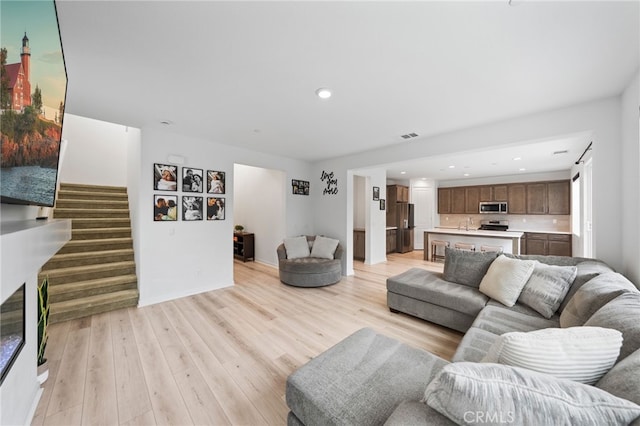 living room with stairs, light wood-style flooring, recessed lighting, and baseboards