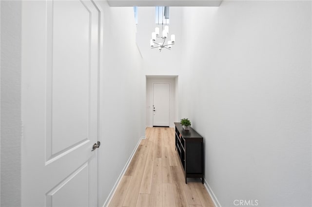 hall with baseboards, a chandelier, and light wood-type flooring