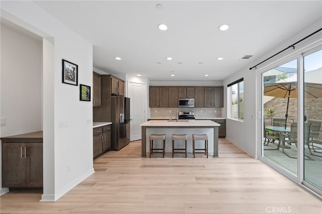 kitchen with stainless steel appliances, light countertops, light wood finished floors, dark brown cabinetry, and recessed lighting
