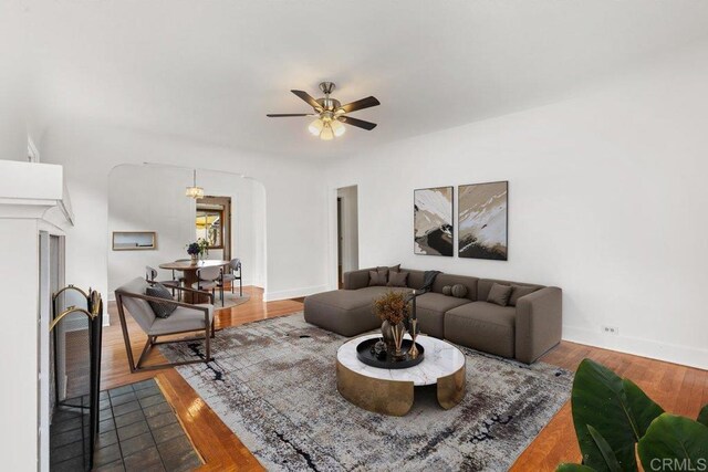 living area featuring a ceiling fan, baseboards, wood finished floors, and arched walkways