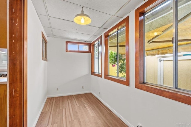 empty room with wood finished floors, a paneled ceiling, and baseboards