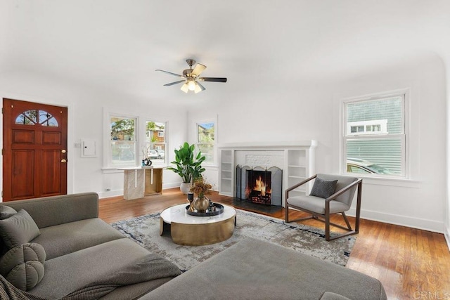 living room featuring ceiling fan, baseboards, wood finished floors, and a fireplace