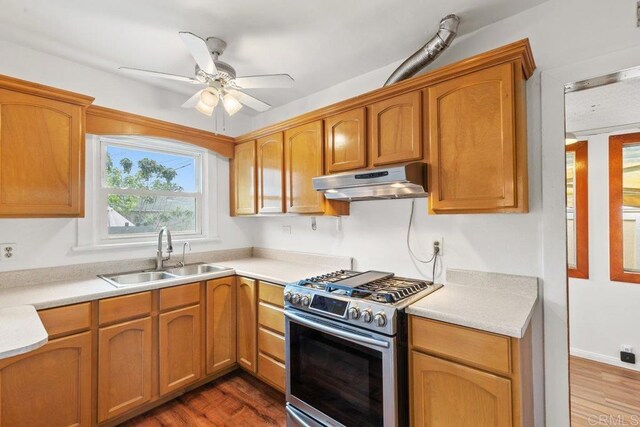 kitchen featuring stainless steel gas range oven, a sink, under cabinet range hood, a ceiling fan, and light countertops