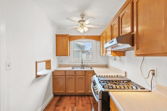 kitchen with under cabinet range hood, stainless steel gas range oven, a sink, ceiling fan, and dark wood-style flooring