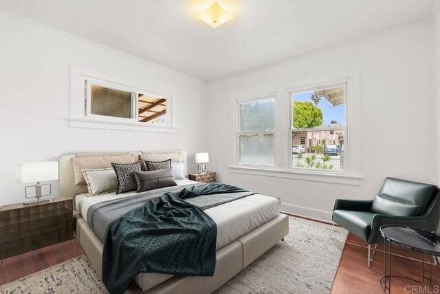 bedroom with ornamental molding, wood finished floors, and baseboards