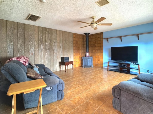 9884 Settle Rd, Santee, CA 92071 - living area with a wood stove, a ceiling fan, wood walls, tile patterned floors, and a textured ceiling