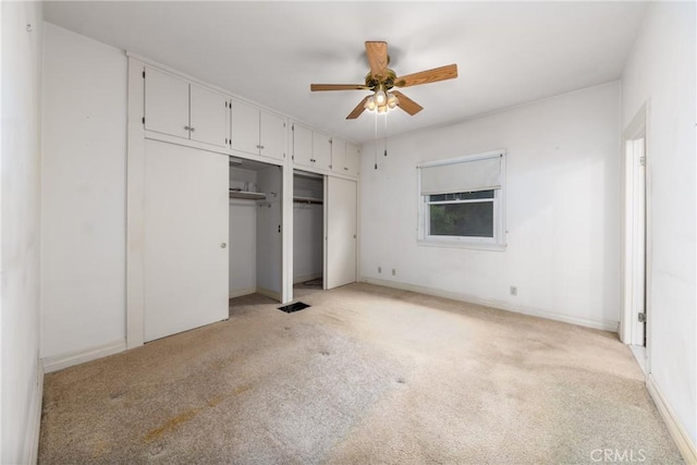 unfurnished bedroom featuring two closets, light carpet, and baseboards