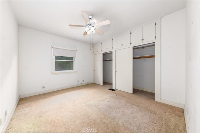 unfurnished bedroom featuring multiple closets, light carpet, baseboards, and ceiling fan