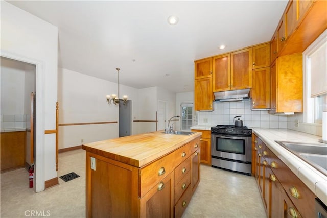 kitchen featuring gas stove, a sink, light flooring, under cabinet range hood, and tasteful backsplash