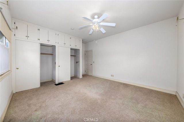 unfurnished bedroom with light colored carpet, multiple closets, a ceiling fan, and baseboards