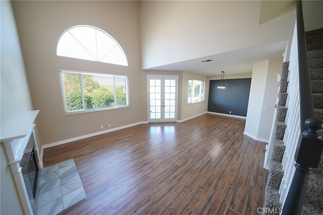 unfurnished living room with wood finished floors, a tile fireplace, baseboards, stairway, and a towering ceiling