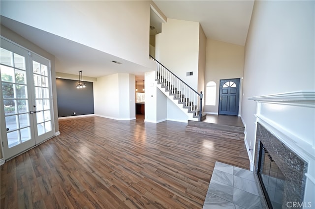 unfurnished living room featuring a towering ceiling, dark wood-style floors, plenty of natural light, and stairs
