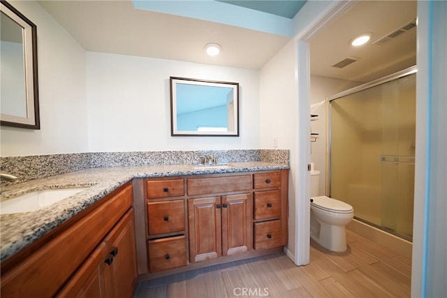bathroom featuring toilet, double vanity, wood finished floors, a stall shower, and recessed lighting