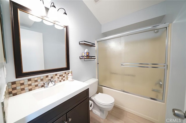 bathroom featuring tasteful backsplash, vaulted ceiling, vanity, toilet, and combined bath / shower with glass door