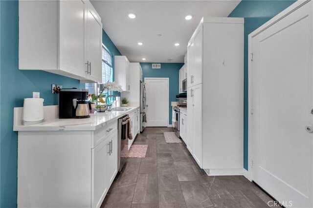 kitchen featuring appliances with stainless steel finishes, white cabinetry, light countertops, a sink, and recessed lighting
