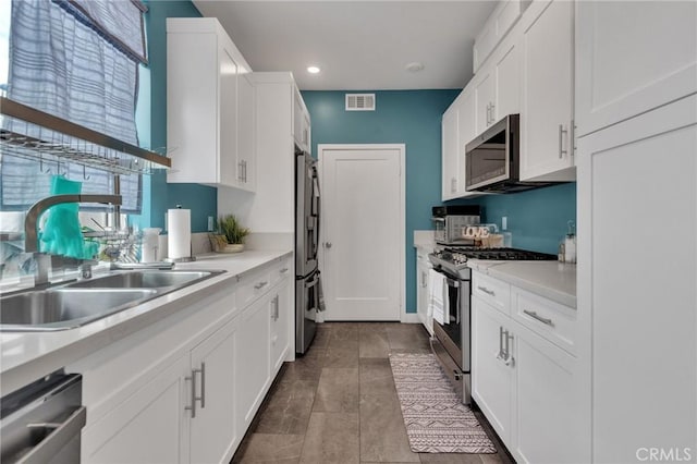 kitchen with appliances with stainless steel finishes, a sink, white cabinetry, light countertops, and recessed lighting