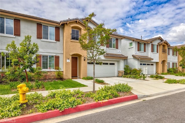 townhome / multi-family property with a garage, stucco siding, driveway, and stone siding