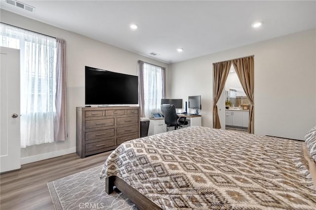 bedroom featuring wood finished floors, recessed lighting, baseboards, connected bathroom, and an office area