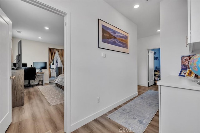 hallway with light wood finished floors, a desk, baseboards, and recessed lighting