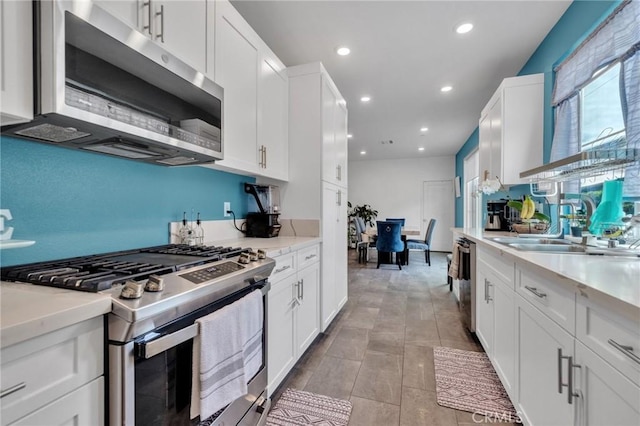 kitchen with stainless steel appliances, light countertops, white cabinets, a sink, and recessed lighting