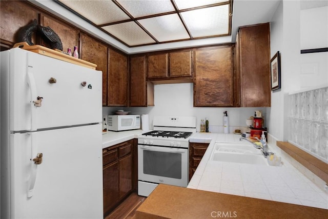 kitchen with white appliances, tile countertops, and a sink