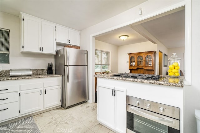 kitchen with appliances with stainless steel finishes, light stone countertops, white cabinetry, a peninsula, and light marble finish flooring