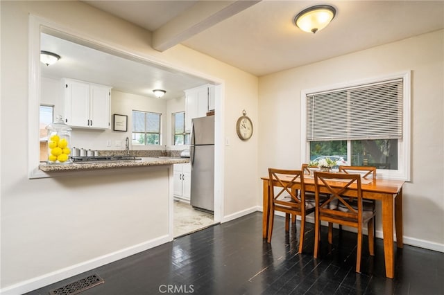 kitchen with freestanding refrigerator, white cabinets, a peninsula, wood finished floors, and beam ceiling