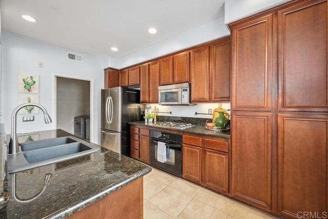 kitchen featuring appliances with stainless steel finishes, a sink, light tile patterned floors, dark stone countertops, and recessed lighting