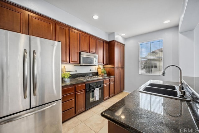 kitchen with appliances with stainless steel finishes, a sink, light tile patterned floors, dark stone counters, and recessed lighting