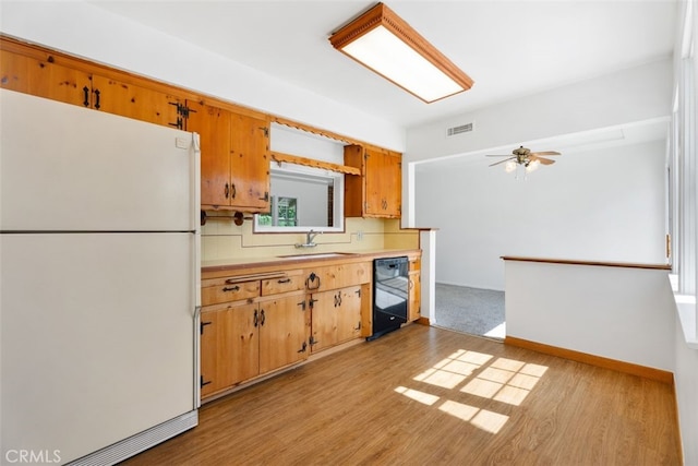 kitchen featuring freestanding refrigerator, black dishwasher, a sink, light countertops, and light wood-type flooring