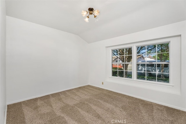 carpeted spare room featuring vaulted ceiling, baseboards, and a chandelier