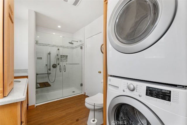 washroom featuring stacked washer / dryer, wood finished floors, and recessed lighting
