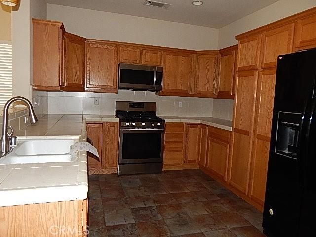 615 Vallecito Way, Red Bluff, CA 96080 - kitchen featuring stainless steel appliances, a sink, tile counters, tasteful backsplash, and brown cabinetry
