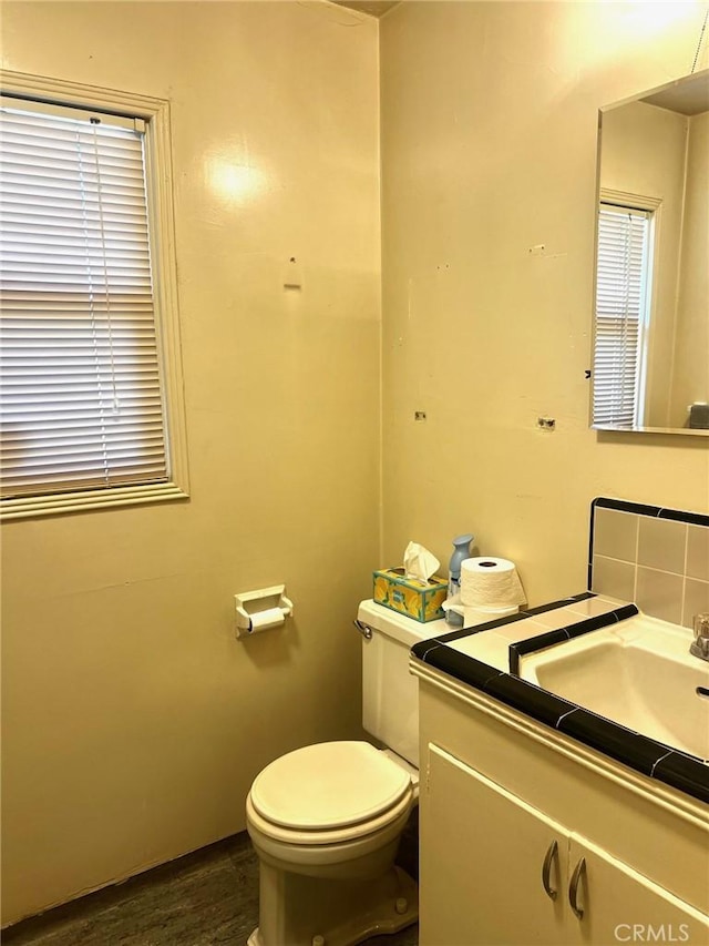 half bath featuring toilet, vanity, decorative backsplash, and wood finished floors