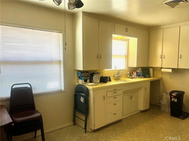 kitchen with a sink, tile countertops, a ceiling fan, light floors, and baseboards
