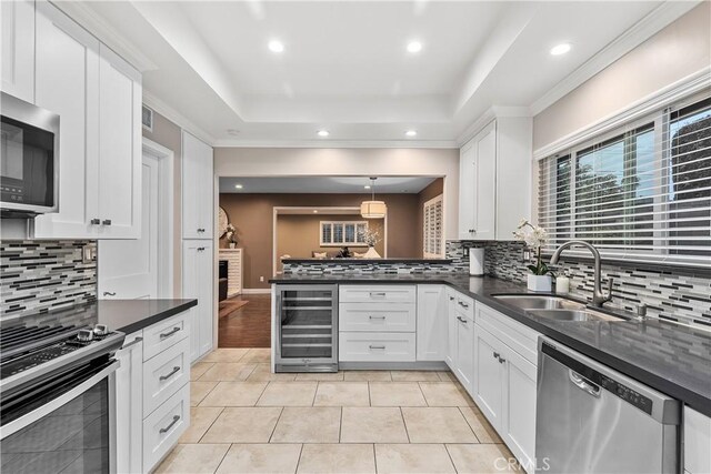 kitchen with appliances with stainless steel finishes, wine cooler, a sink, a tray ceiling, and dark countertops