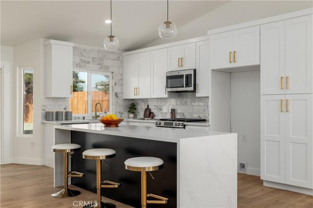 kitchen with stainless steel microwave, lofted ceiling, backsplash, a center island, and light countertops