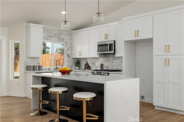 kitchen featuring stainless steel microwave, vaulted ceiling, tasteful backsplash, a center island, and light countertops