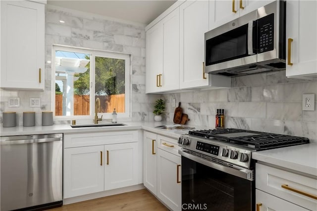 kitchen featuring appliances with stainless steel finishes, a sink, light countertops, white cabinets, and decorative backsplash