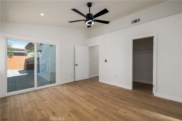 unfurnished bedroom featuring access to exterior, baseboards, light wood-type flooring, a walk in closet, and vaulted ceiling