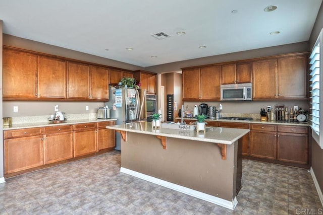 kitchen featuring appliances with stainless steel finishes, brown cabinets, a breakfast bar, an island with sink, and recessed lighting