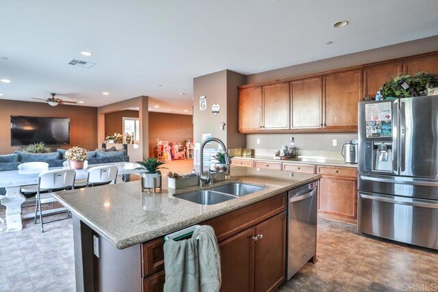 kitchen with stainless steel appliances, a sink, a center island with sink, light stone countertops, and open floor plan