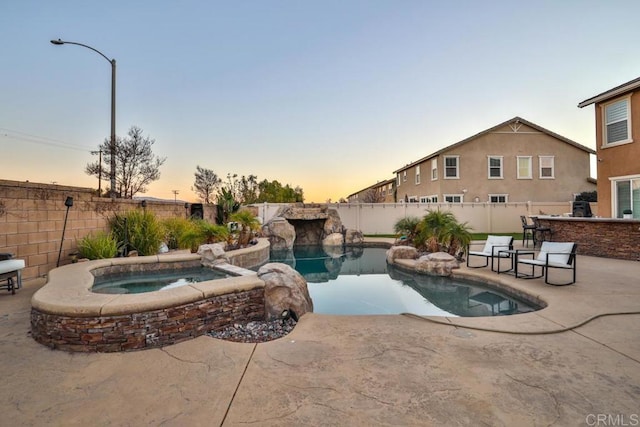 pool at dusk with a patio area, a fenced backyard, and a pool with connected hot tub