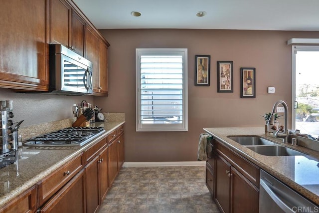 kitchen with appliances with stainless steel finishes, a sink, stone countertops, baseboards, and recessed lighting