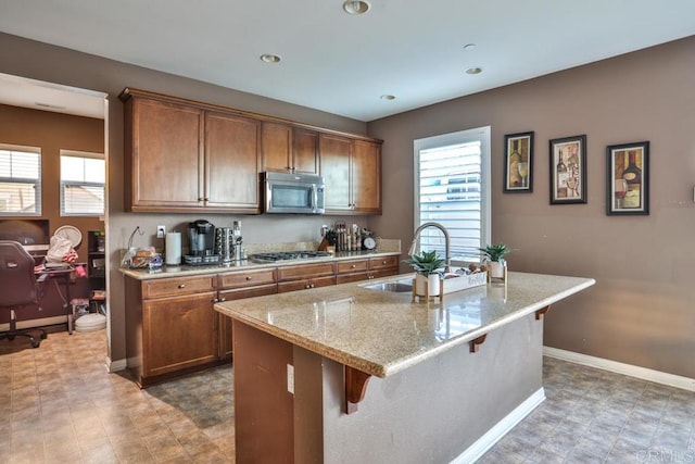 kitchen with a sink, stainless steel appliances, brown cabinetry, a kitchen breakfast bar, and a center island with sink
