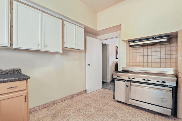 1703 W 25th St, Los Angeles, CA 90018 - kitchen with under cabinet range hood, stainless steel gas stove, decorative backsplash, dark countertops, and white cabinetry