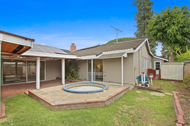 back of property with an in-ground hot tub, solar panels, a patio area, and stucco siding